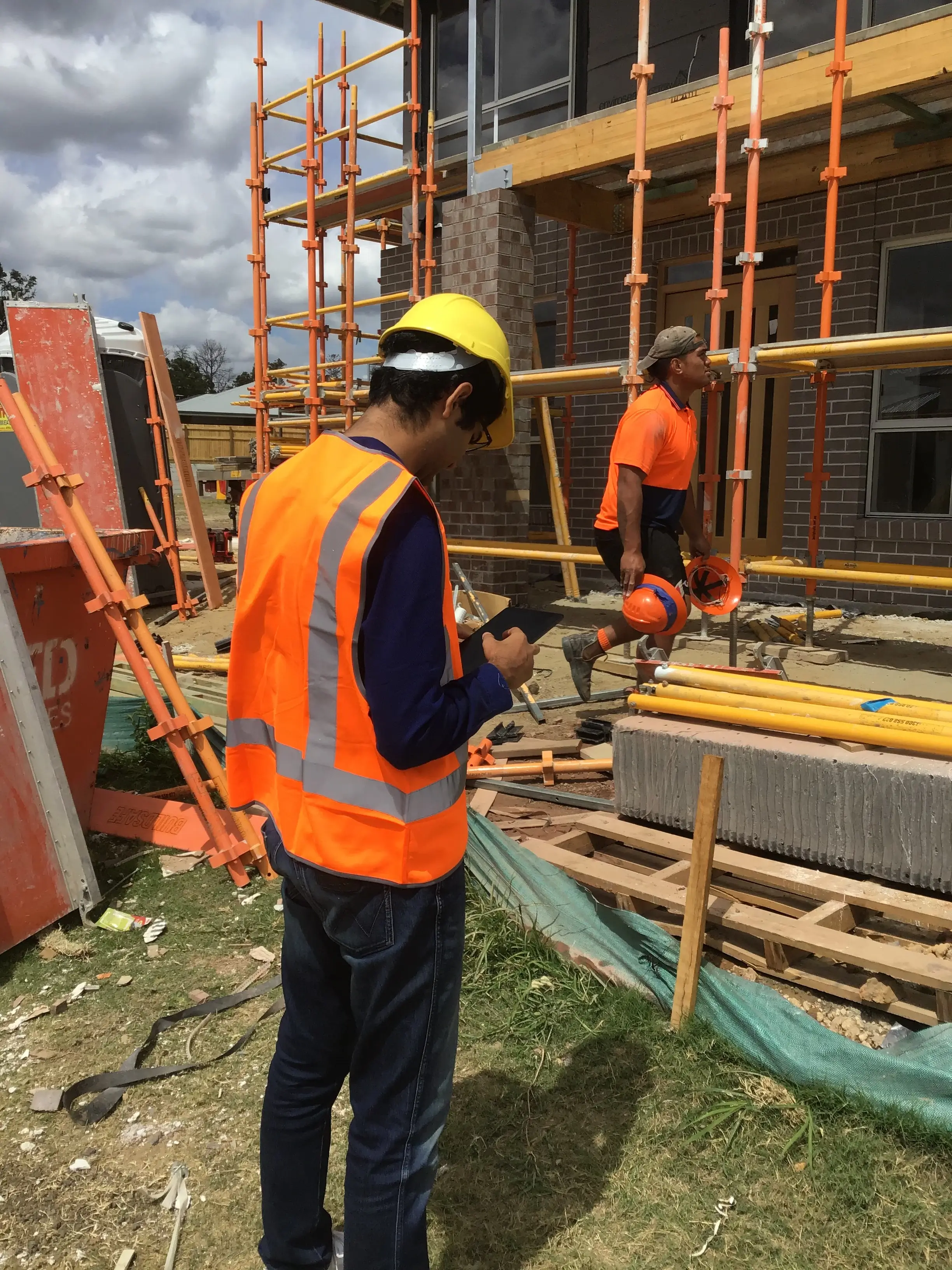 Image of two trades people at a construction site, one holding a tablet